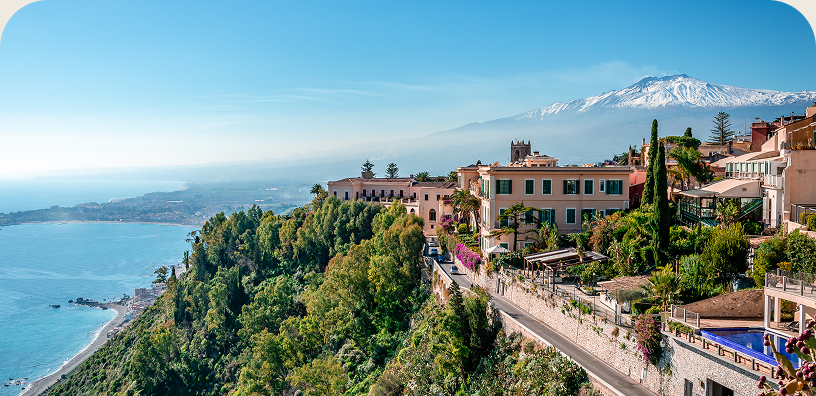 Coastal hillside town overlooking the sea with Mount Etna in the distance