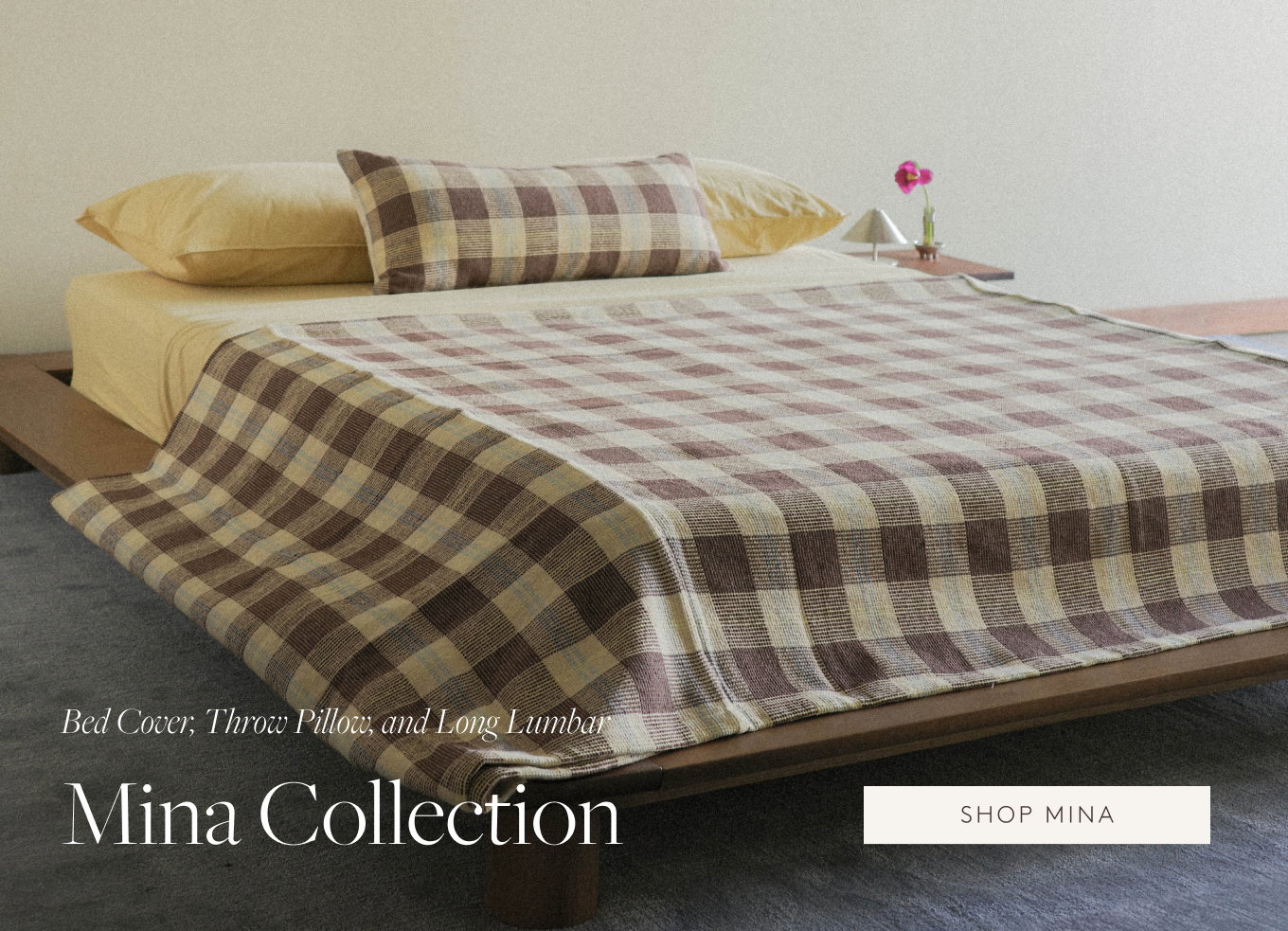 Brown check quilt and lumbar pillows with soft yellow sheets on a bed.