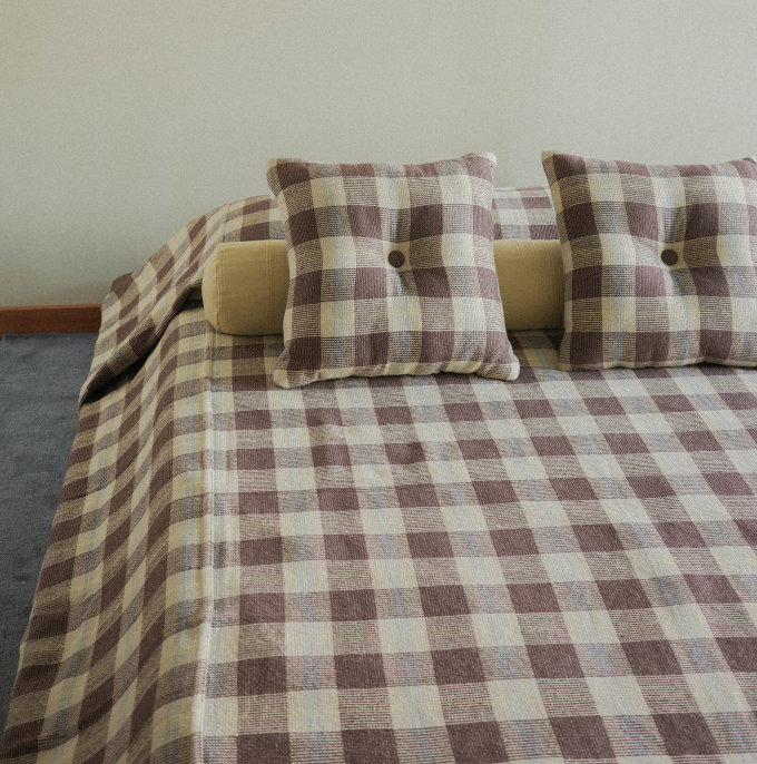 Two brown check square pillows on top of a brown check quilt