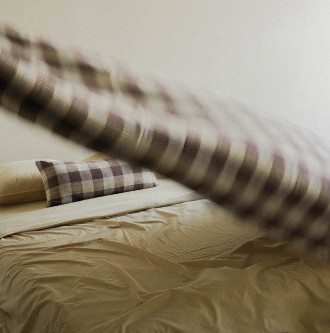 Blurry shot of a brown check quilt in motion over a bed