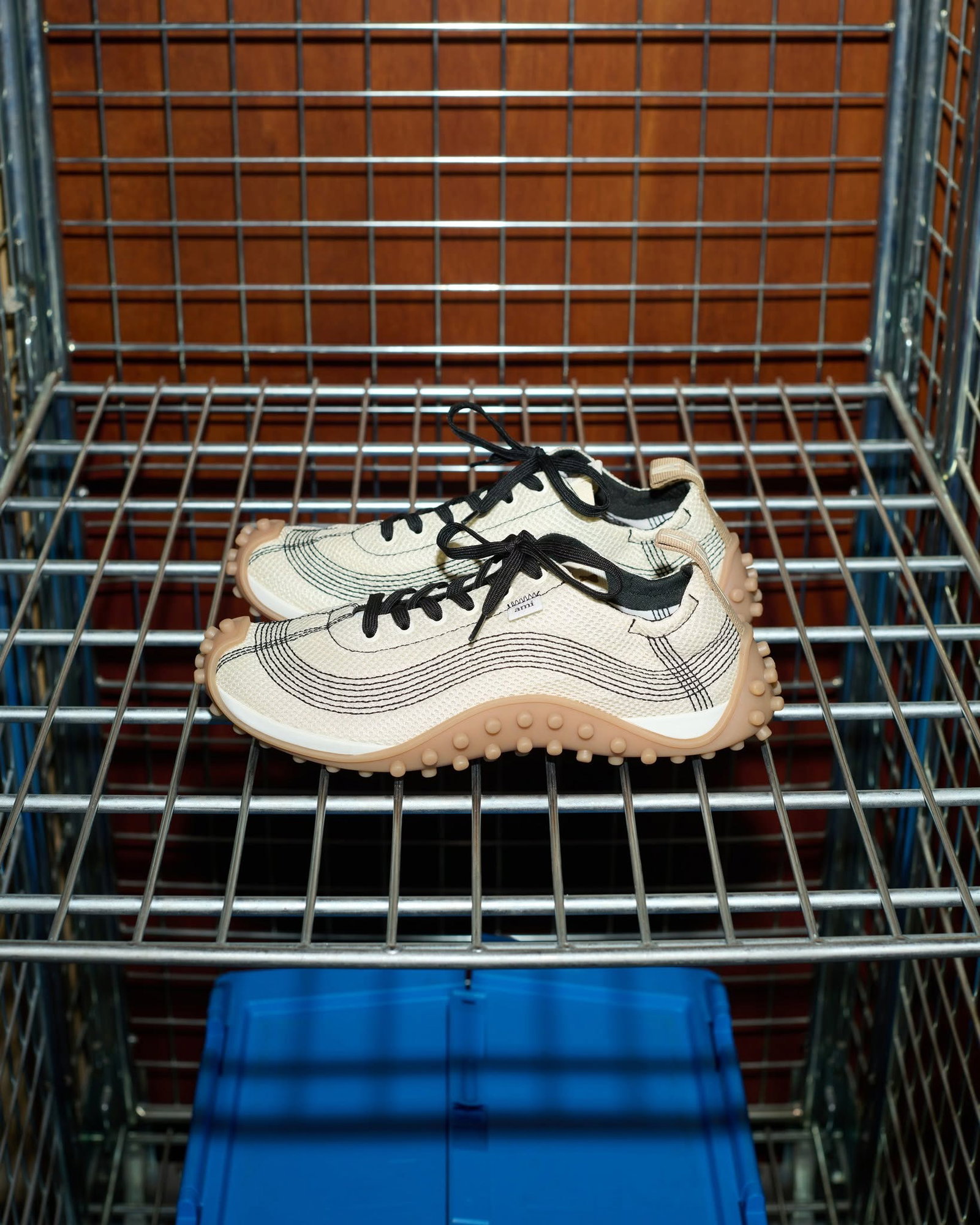 Pair of beige woven trainers with black laces and studded gum soles displayed on a metal wire shelf