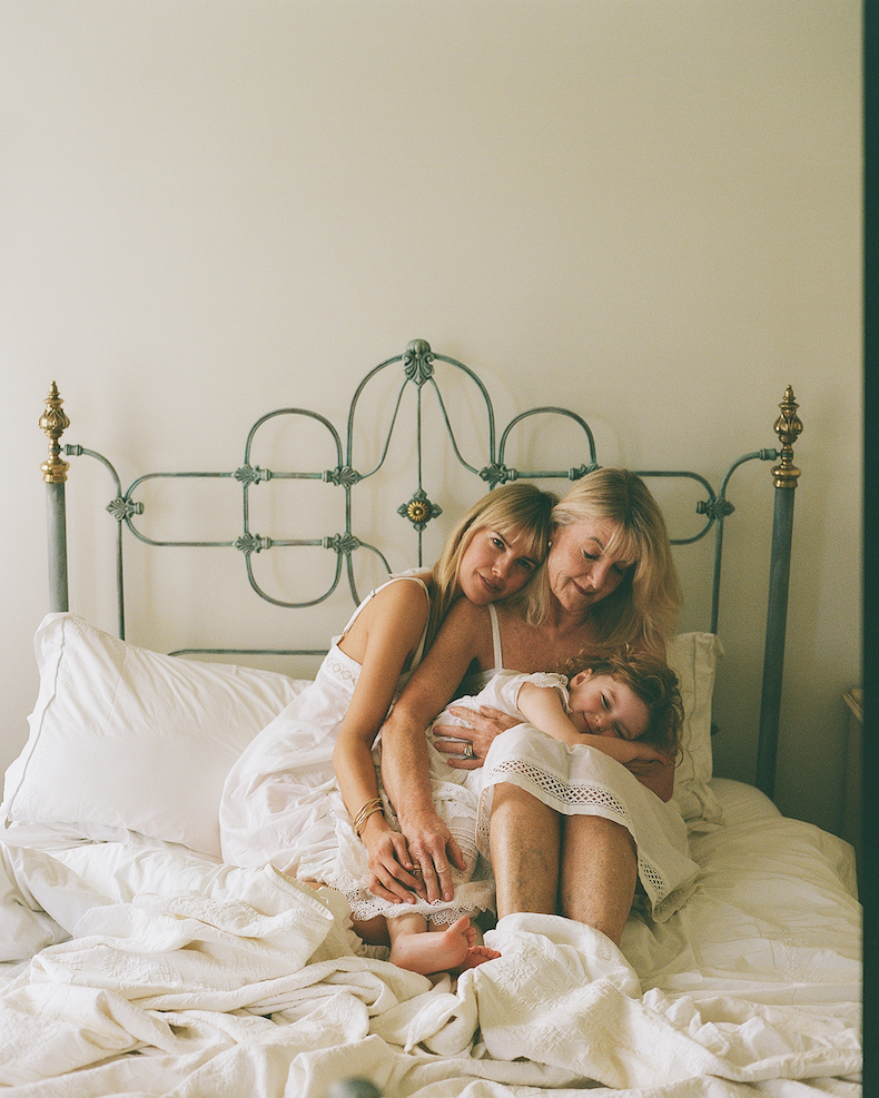 Molly, her mum and her children cuddled up together in bed, dressed in soft white sleepwear.