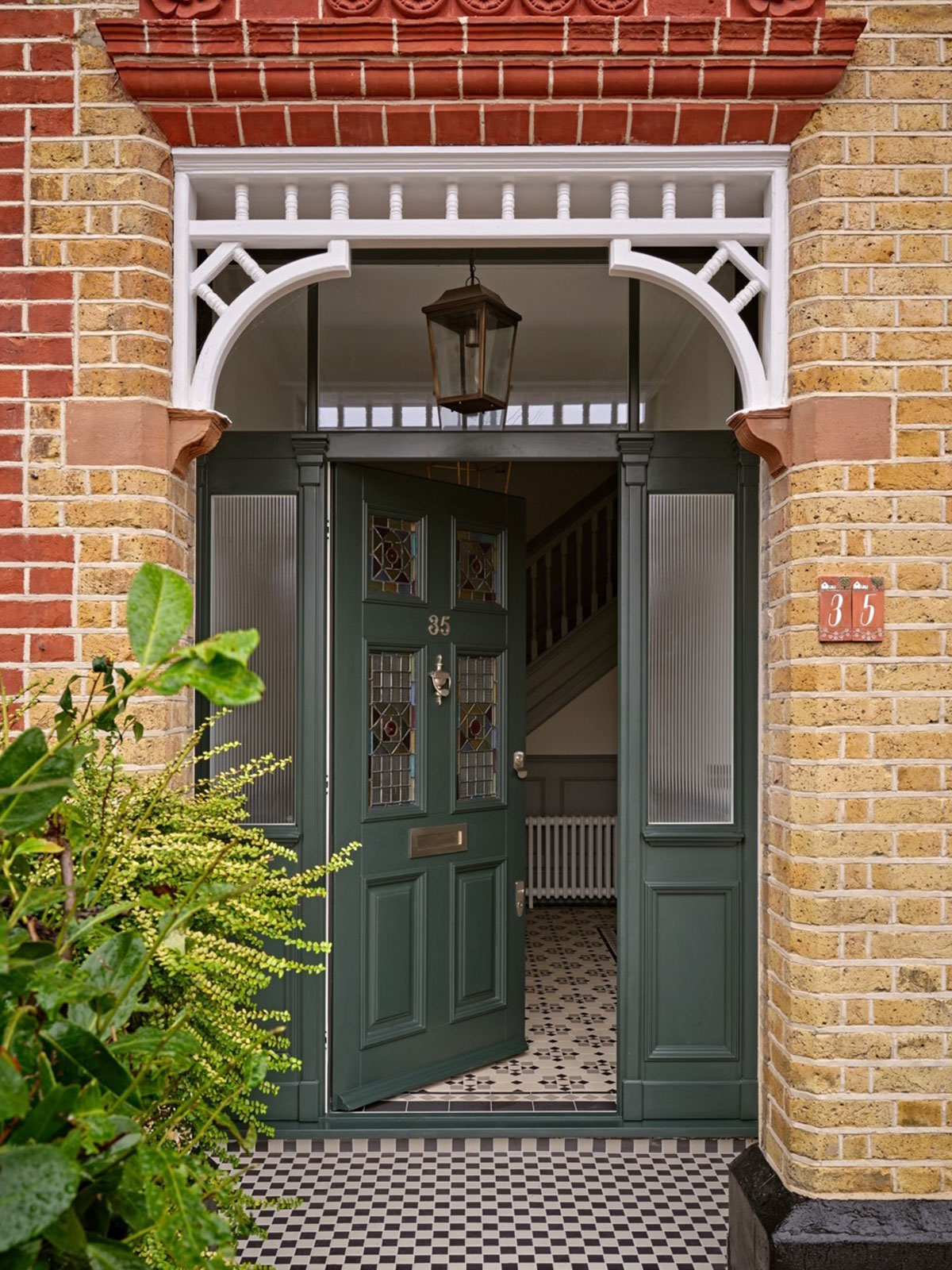 A dark green door with stained‑glass panels, partially open, set in detailed brickwork with a checker‑tiled entrance.
