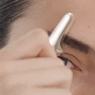 Eye close-up of a person gliding the Rejuvenating Eye Tool outward along the brow’s natural arch.