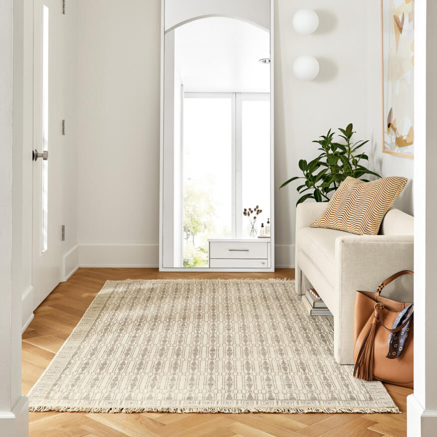 Soho arched mirror leans in an entryway with a rug, bench, and plant nearby.