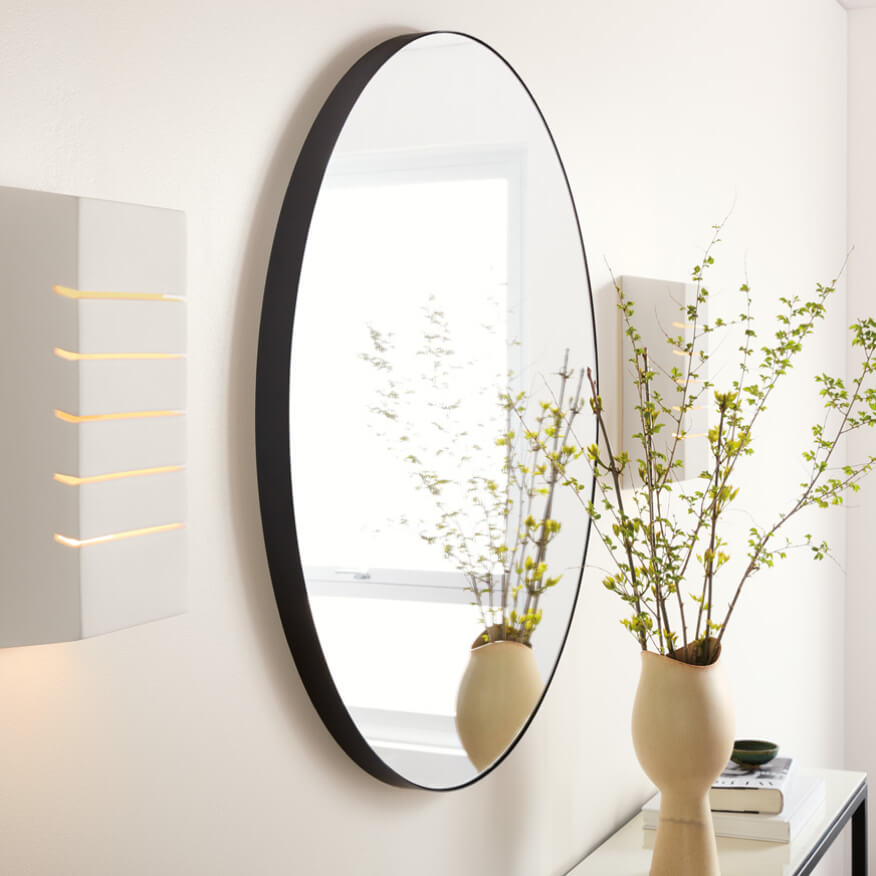 Gamma round mirror with a black frame above a console table with books and a vase.