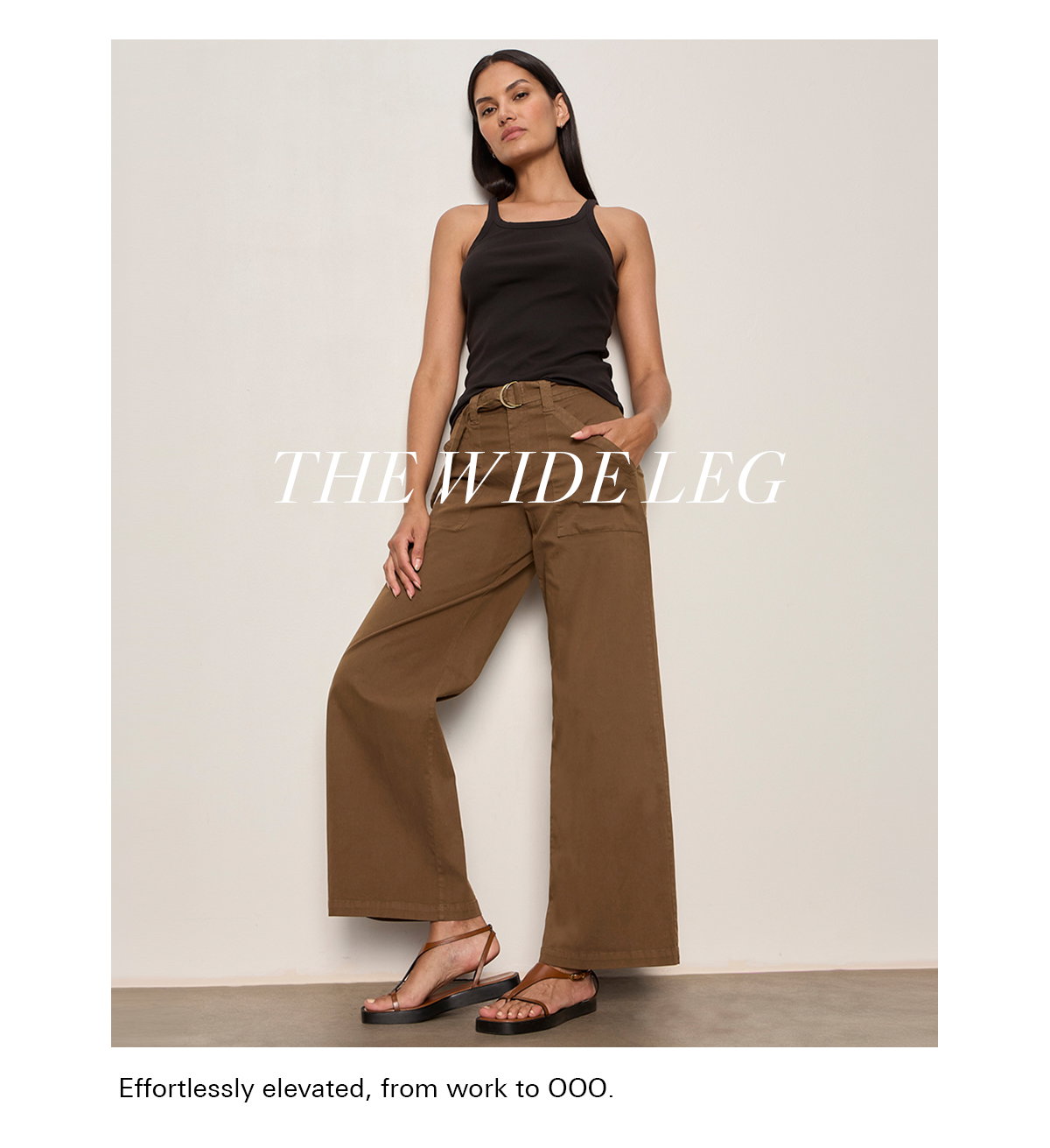 A woman stands confidently against a plain wall, wearing a black sleeveless top, high-waisted wide-leg brown pants with a belt, and black sandals. Text on the image reads "THE WIDE LEG.