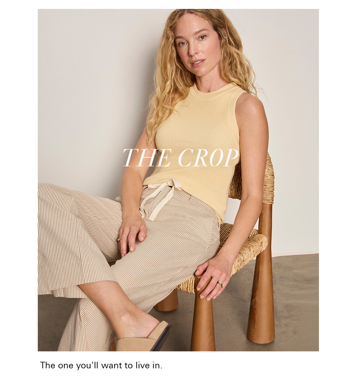 A woman with wavy blonde hair sits on a wooden chair, wearing a sleeveless, pale yellow ribbed crop top and beige striped pants. The text "THE CROP" overlays the image. The caption below reads: "The one you'll want to live in.