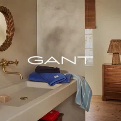 Salle de bain avec des murs beige, un miroir en corde courbe, un robinet en laiton, des serviettes empilées (bleu, marine et rayé), une commode en bois et une lampe tissée.