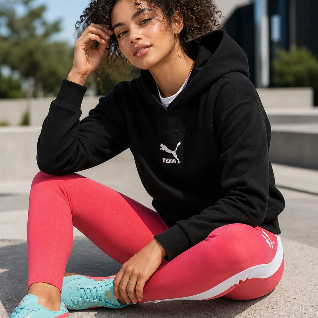 Woman in black PUMA hoodie and pink leggings crouching outdoors wearing blue sneakers