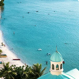 A high-angle view of a tropical beach with turquoise water, colorful kayaks on the sand, and a domed building in the foreground.