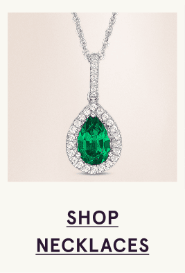 A white metal necklace with a diamond and emerald pendant. Click here to shop necklaces