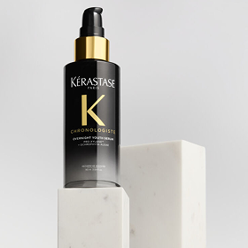 Flacone di Kérastase Chronologiste Overnight Youth Serum su basamento in marmo bianco, sfondo grigio chiaro