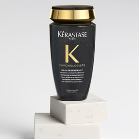 Flacone di shampoo Kérastase Chronologiste Bain Régénérant nero e oro su blocchi di marmo bianco