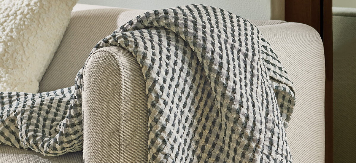 Striped textured throw arranged on beige sofa arm beside ivory accent cushion.