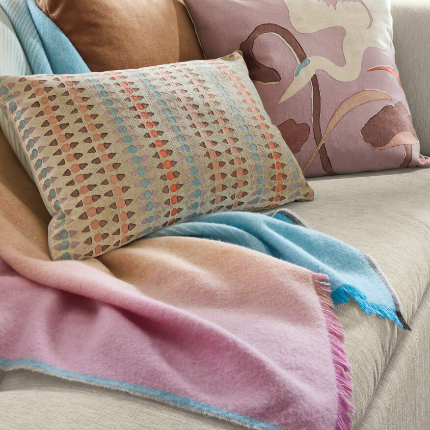 Colburn throw with multicolour pattern and fringe, layered on a sofa with decorative pillows.