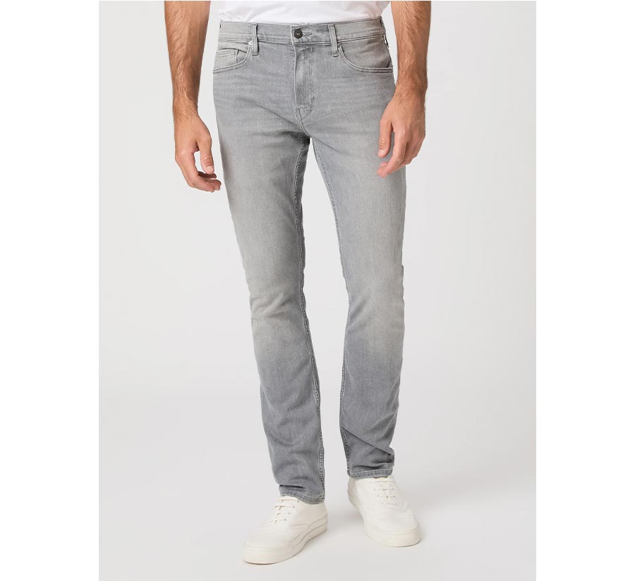 Man wearing a pair of slim straight-fit grey jeans with a white tee and cream sneakers in front of a grey backdrop.