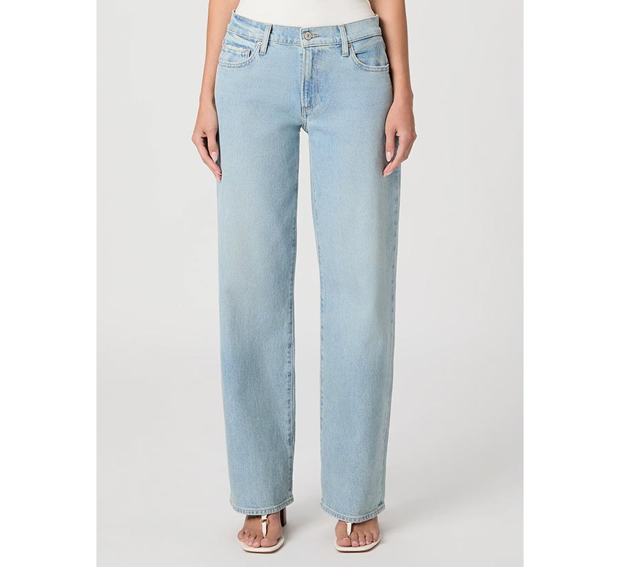 Woman wearing a pair of light wash low-rise straight-leg jeans with a white tank and white heeled sandals in front of a grey backdrop..