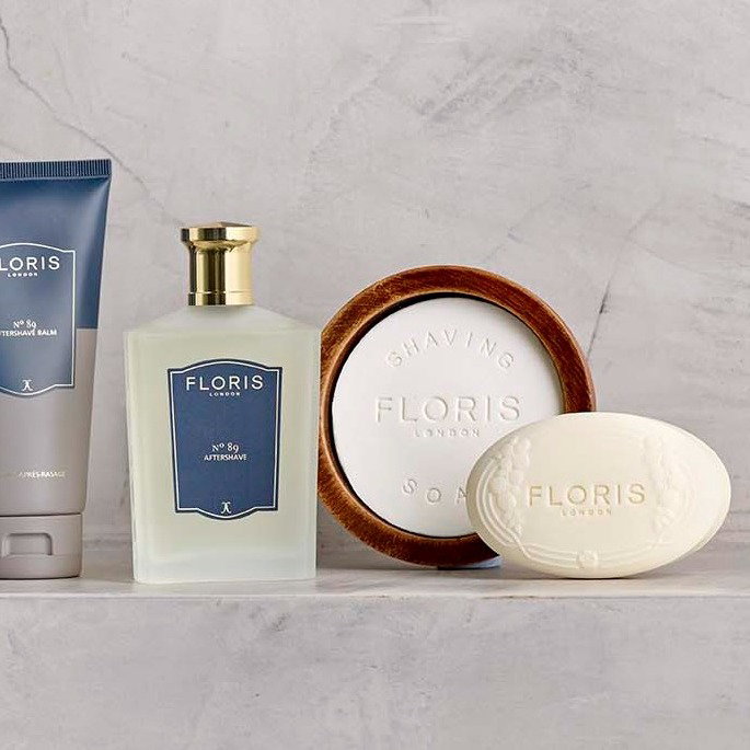 A collection of Floris grooming products, including Aftershave and a shaving bowl stand against a grey textured background