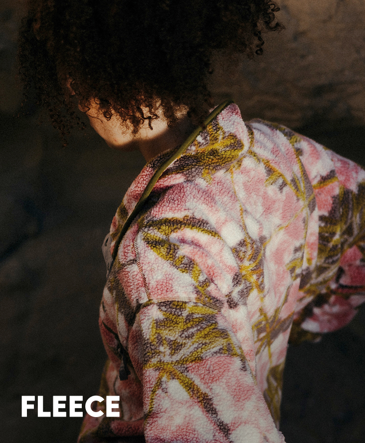 A woman wearing a pink and green floral fleece pullover with text: FLEECE