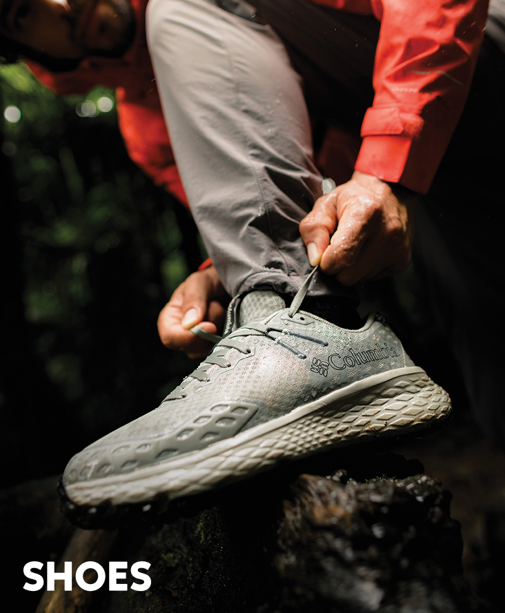 Close-up of a man tying his grey hiking shoes on a rock out in the forest with text: SHOES