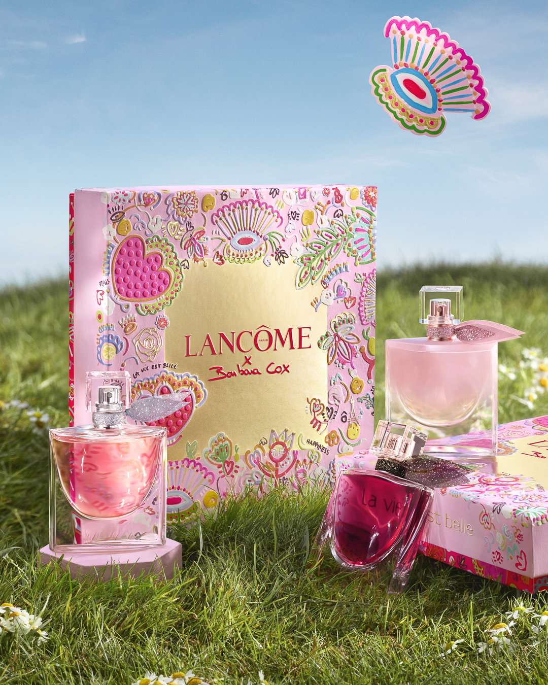 Cofanetto con tre profumi La Vie Est Belle, decorato con illustrazioni floreali colorate su sfondo rosa e oro.
