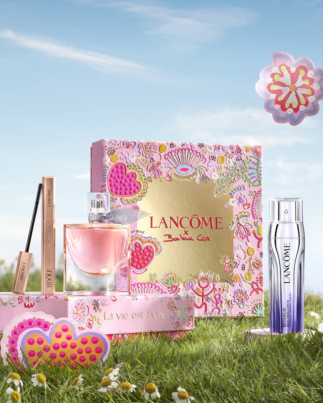 La vie est belle Eau de Parfum, mascara Idôle Flutter Extension e Rénergie H.C.F. Triple Serum Lancôme, fotografati su un prato fiorito in un'atmosfera primaverile.