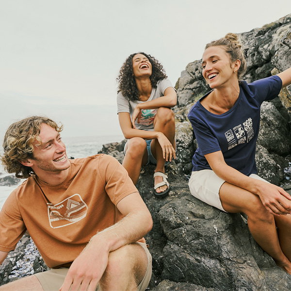 Friends sit on the beach, each sporting a colourful graphic t-shirt.