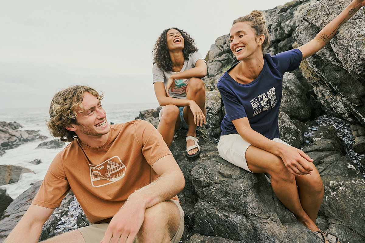 Friends sit on the beach, each sporting a colourful graphic t-shirt.