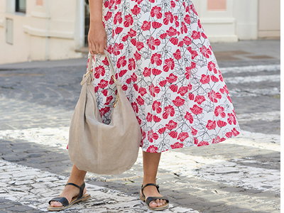 Ein Model trägt ein ecru-gemusterts Kleid mit rotem floralem Print. Daneben folgender Text: Kleider die dich strahlen lassen