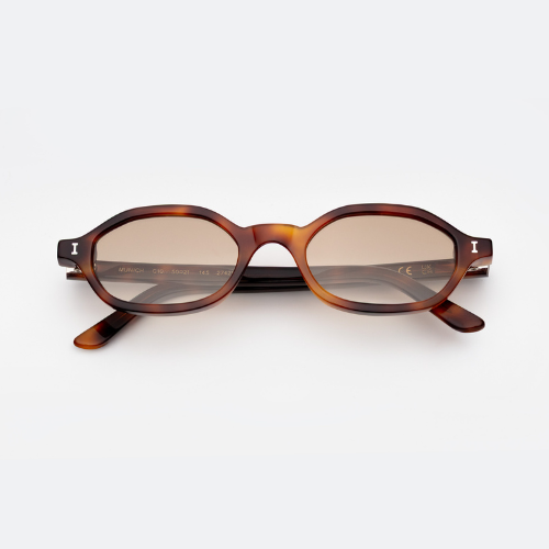 A studio product shot of the Munich sunglasses. These feature a narrow, angular oval frame in a vibrant tortoise-shell pattern with brown tinted lenses and silver 