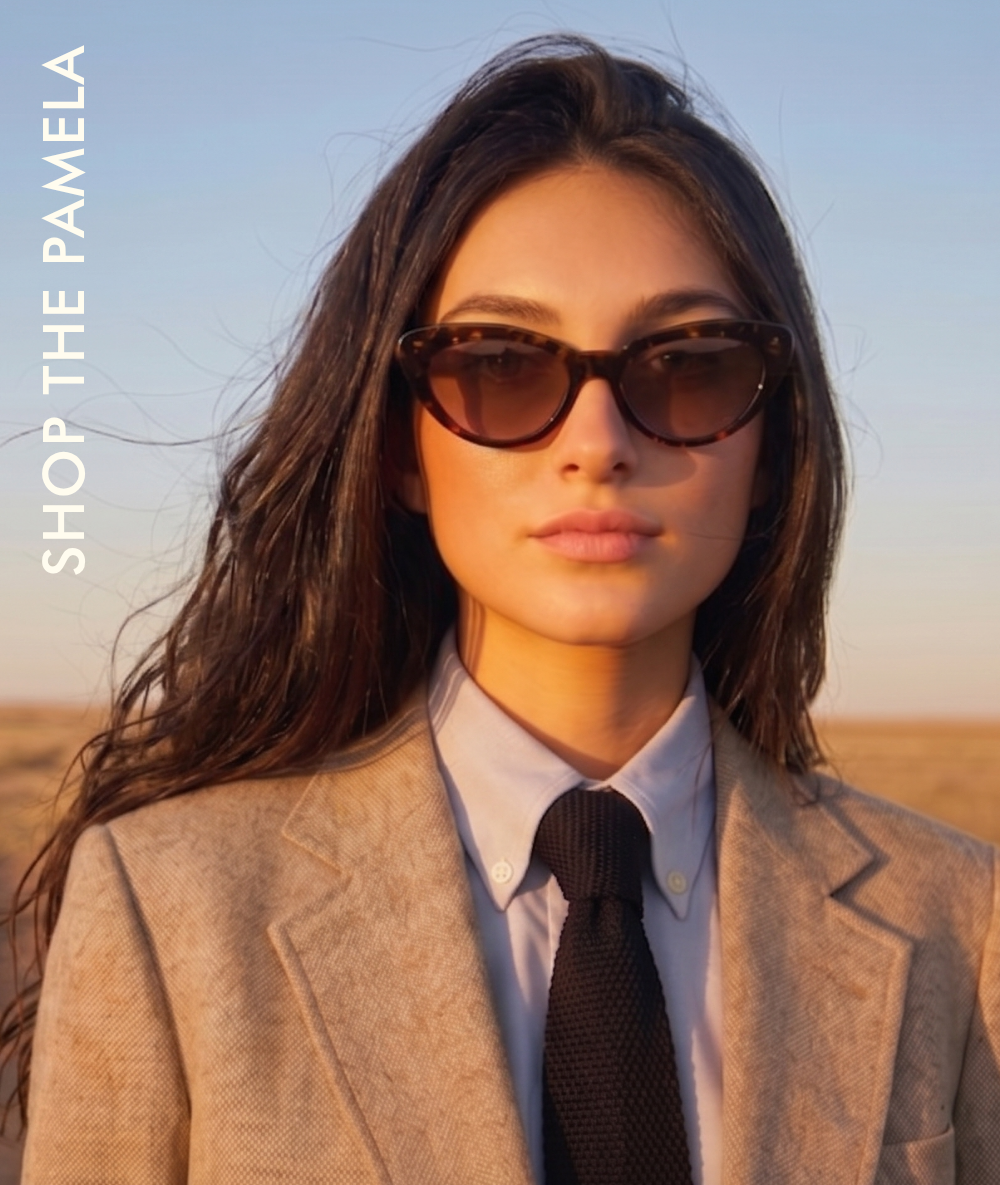 A lifestyle shot of a woman looking off to the side against a clear blue sky. She is wearing the Sheila sunglasses, which feature a translucent brown, 90s-inspired oval frame. She is dressed in a classic olive green trench coat over a white top. The text reads: 