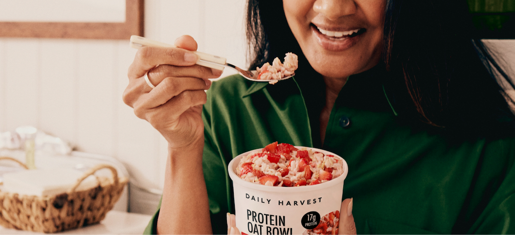 Daily Harvest Protein Oat Bowl with strawberry topping, held in hand as a spoonful is raised.