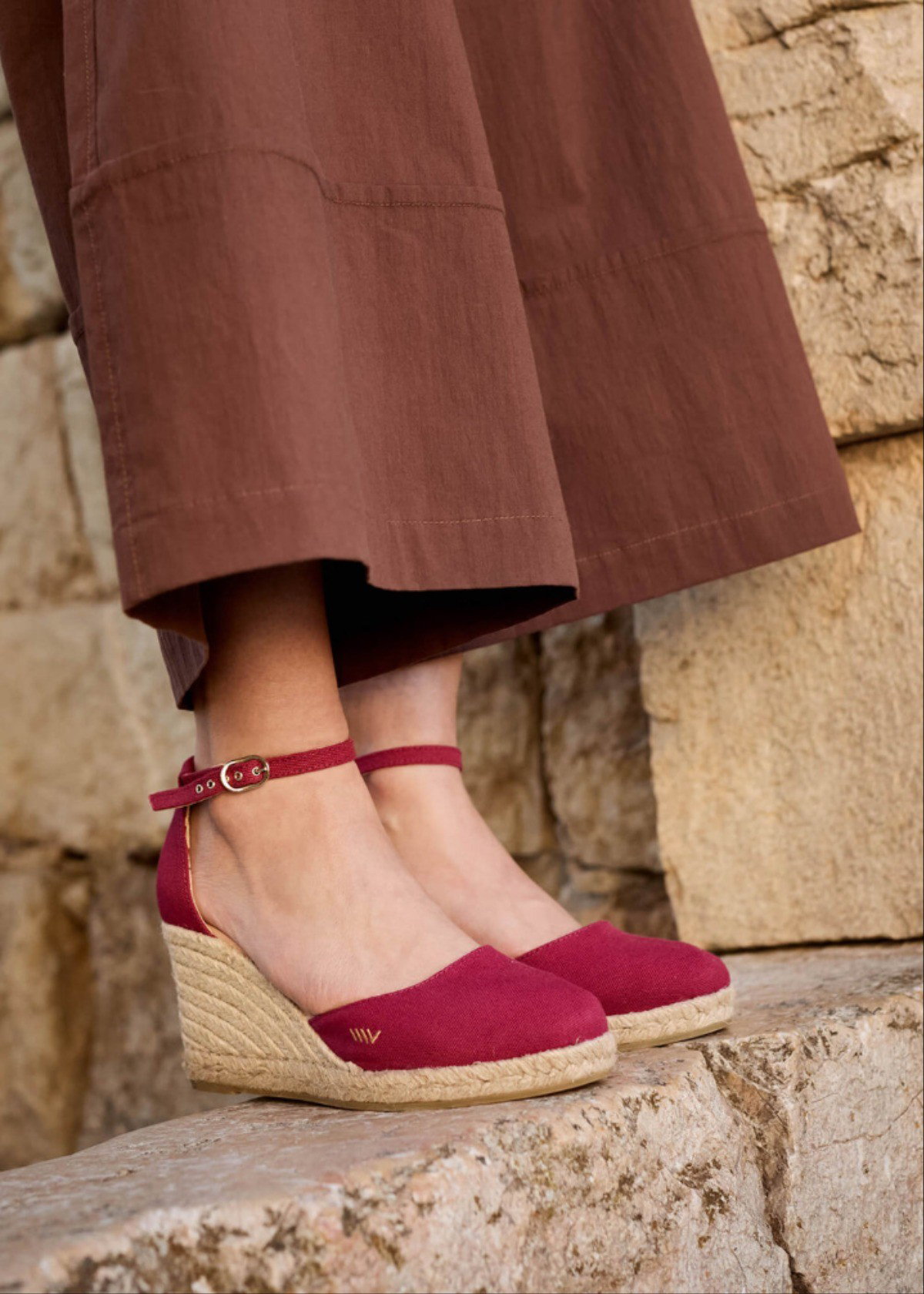 Cherry red espadrille wedges with ankle strap worn on model, styled on stone steps outdoors.