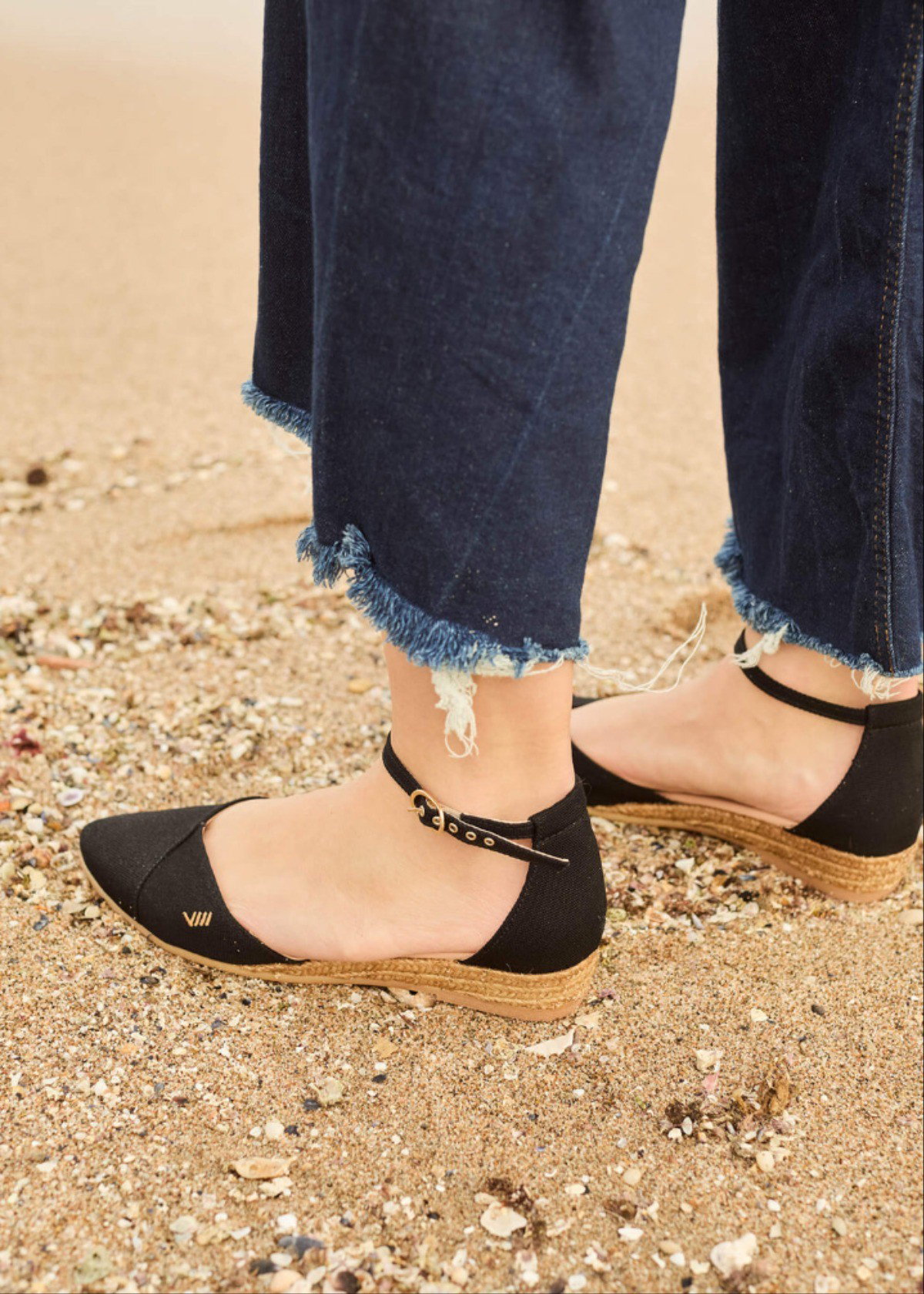 Black espadrille flats with ankle strap worn with cropped denim in a natural outdoor setting.