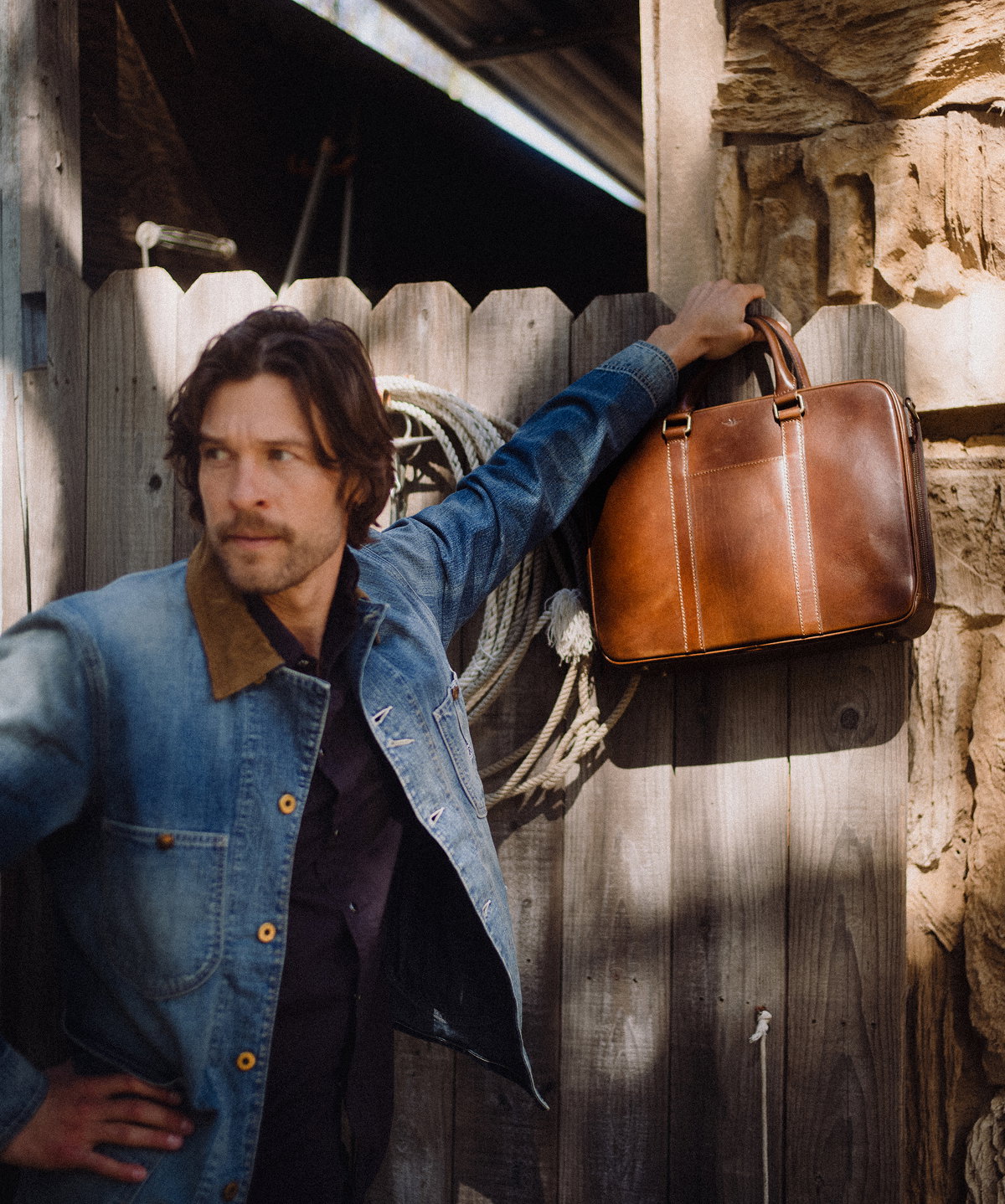 Brown leather briefcase hanging against a wooden fence, highlighting structured shape and rich leather texture