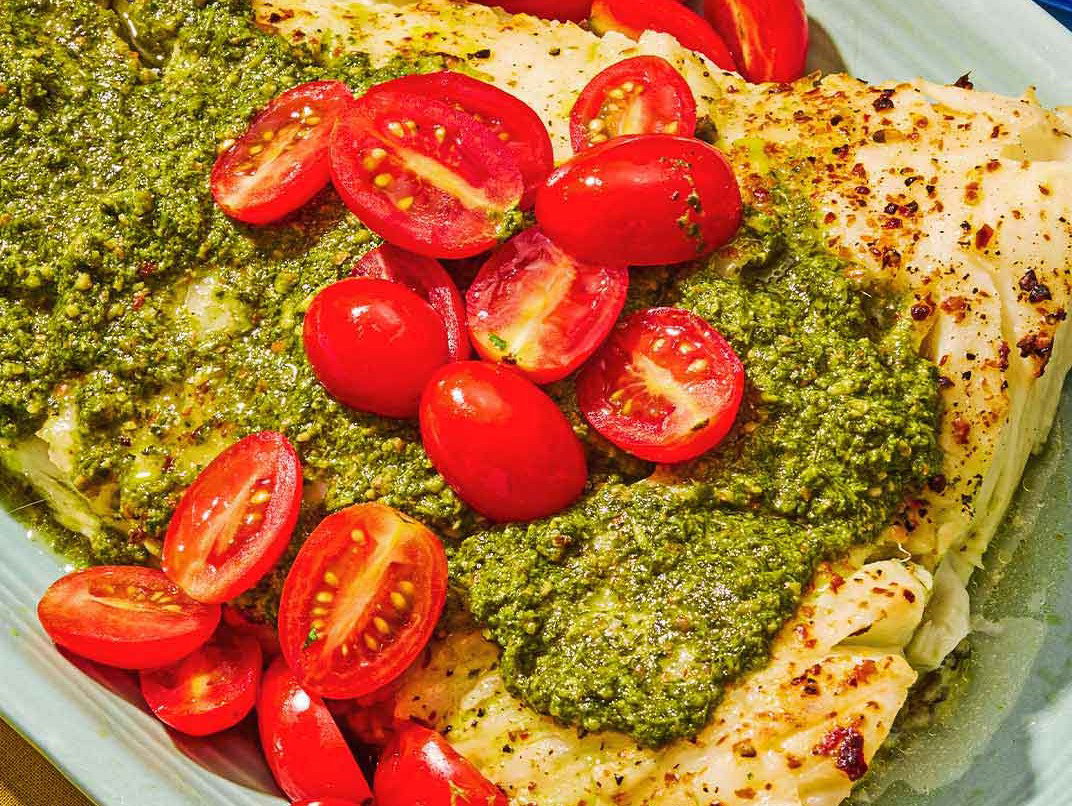 Baked Chilean Sea Bass topped with Pesto and Cherry Tomatoes on a platter.