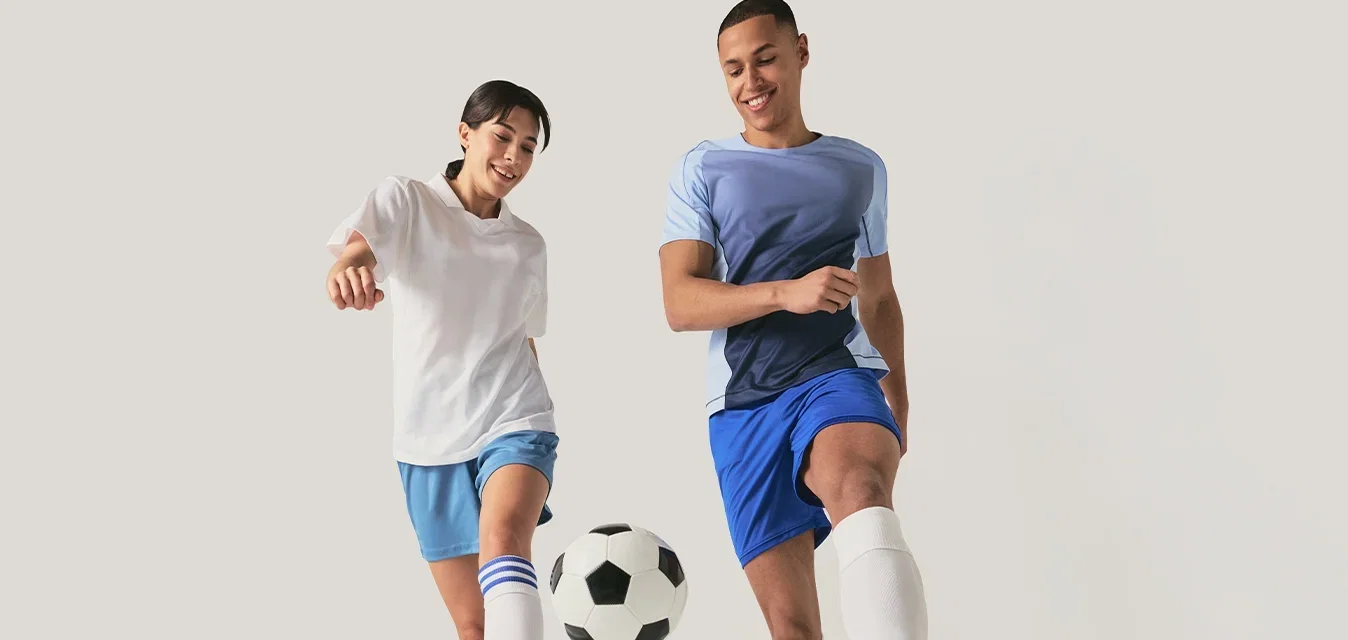 Deux jeunes portant des vêtements de sport frappant ensemble un ballon de football sur un fond clair.