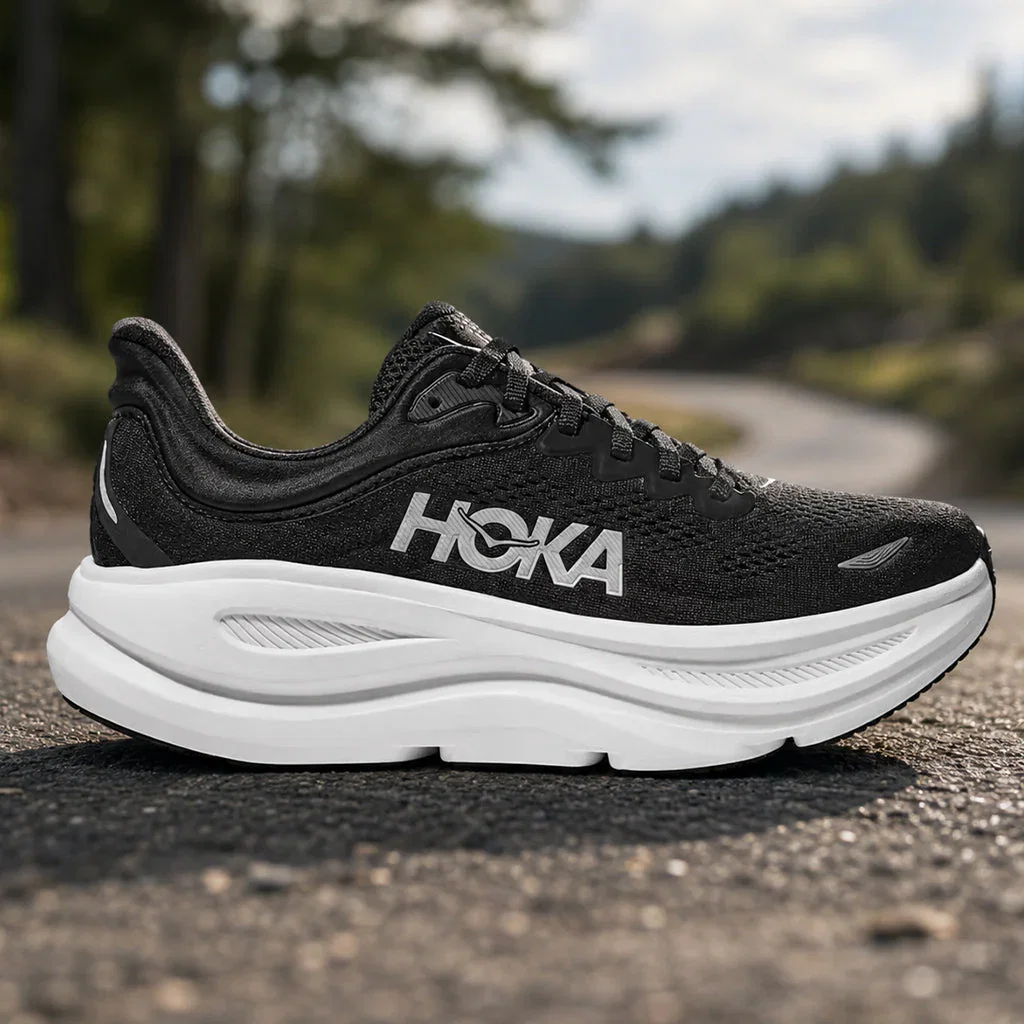 Black and white HOKA running shoe displayed on pavement with scenic mountain landscape and forest in background.