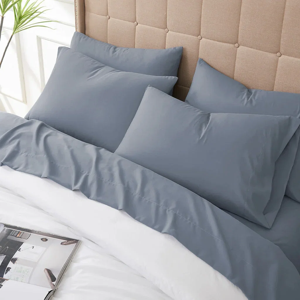 Soft gray sheet set with pillows arranged on bed with beige upholstered headboard and potted plant