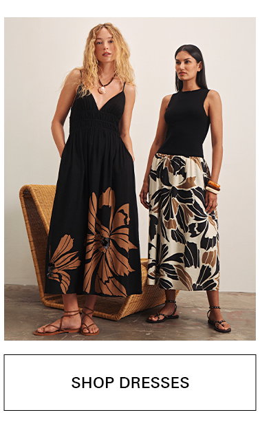 Two women pose in stylish dresses with bold floral prints. One wears a black sleeveless dress with tan floral design; the other wears a black sleeveless top and a cream skirt with black and tan floral patterns. Text reads "SHOP DRESSES.