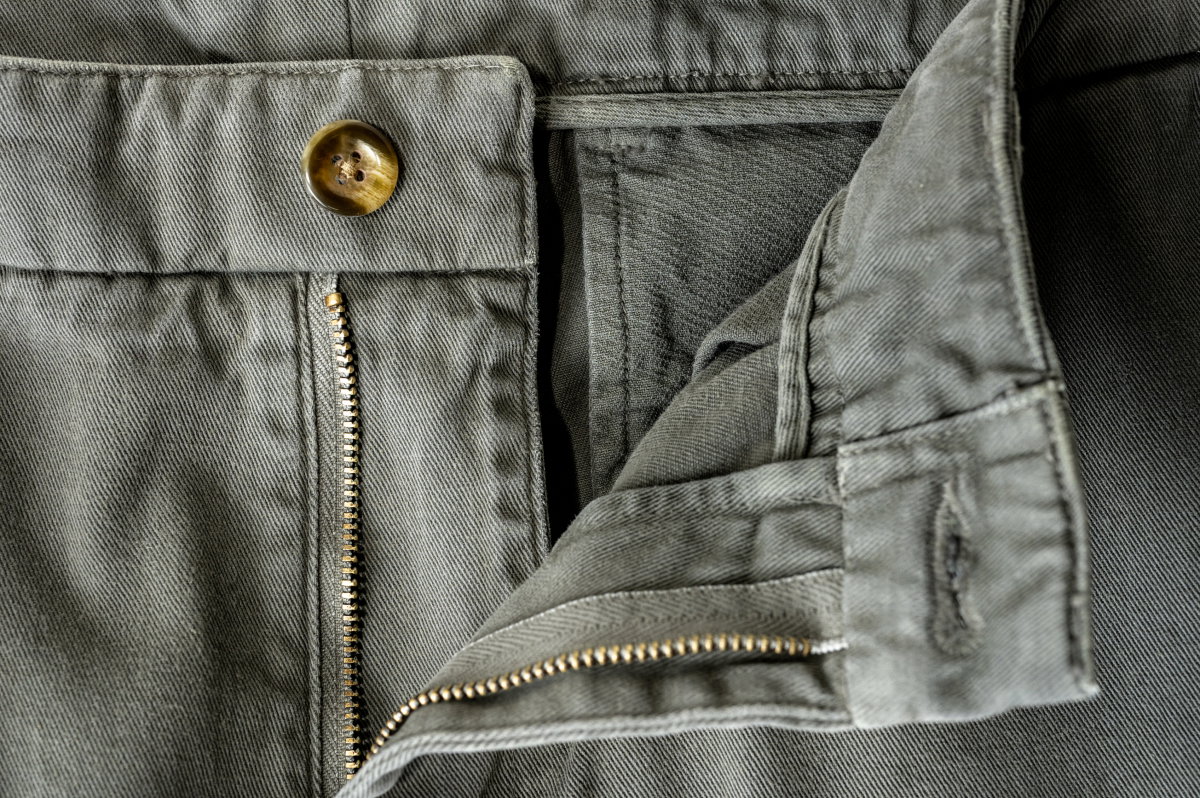A closeup of the open button and zipper of Bills Khakis shorts in olive