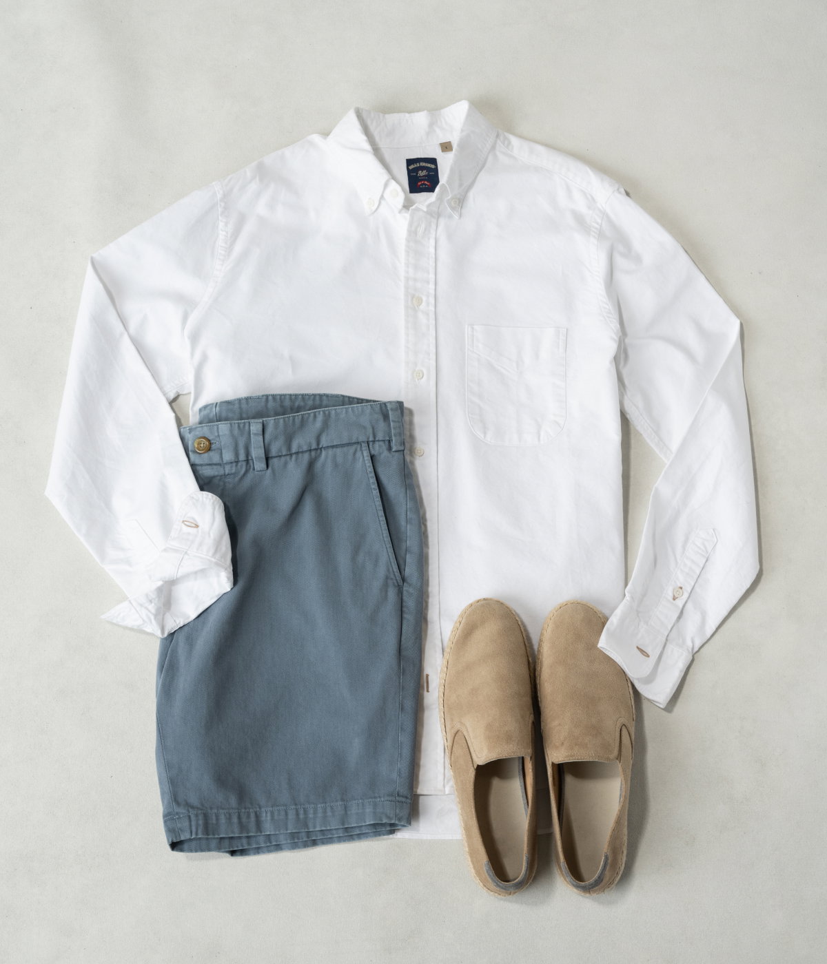 A white Bills Khakis Gitman shirting laying on a warm surface with Bills shorts and a pair of slip on loafers