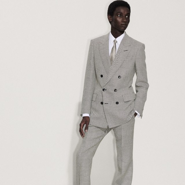Person in a double-breasted gray suit with a white shirt and tie, standing against a plain background.