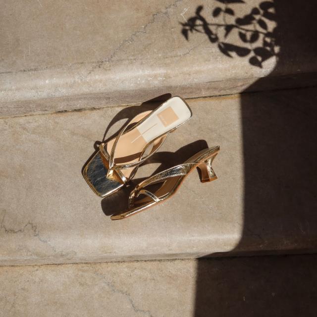 Gold heeled sandals on sunlit stone steps with leaf shadows.