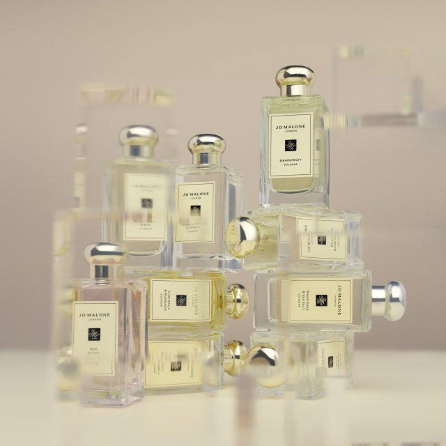 A collection of Jo Malone perfume bottles stacked on a reflective surface, with a soft beige background.