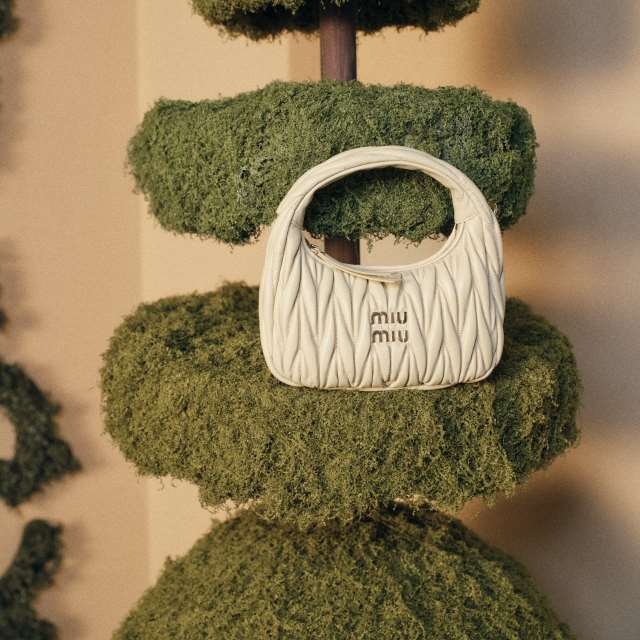 A small, white Miu Miu handbag placed on green, textured topiary plants.