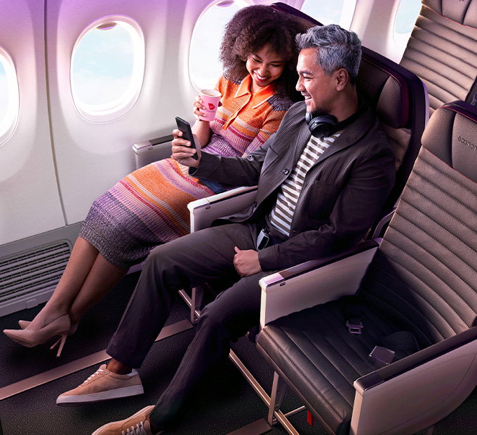 Couple laughing and smiling at each other on a plane in an Economy X seat