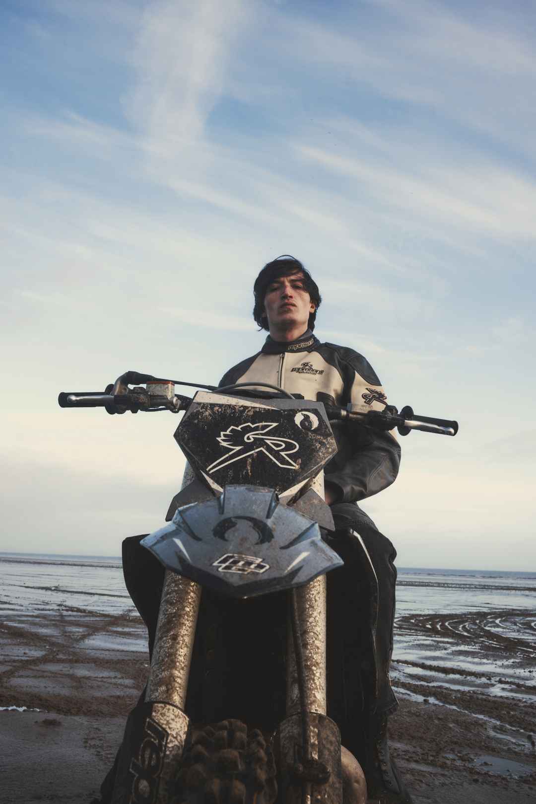 Model riding branded motorcross bikes across a welsh beach in Represent x Belstaff