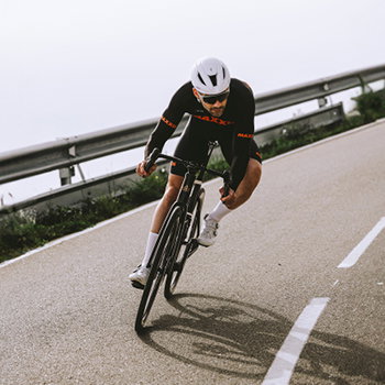 Cyclist in black racing kit and white helmet cornering on a road bike down a coastal bend, high speed, leaning into turn